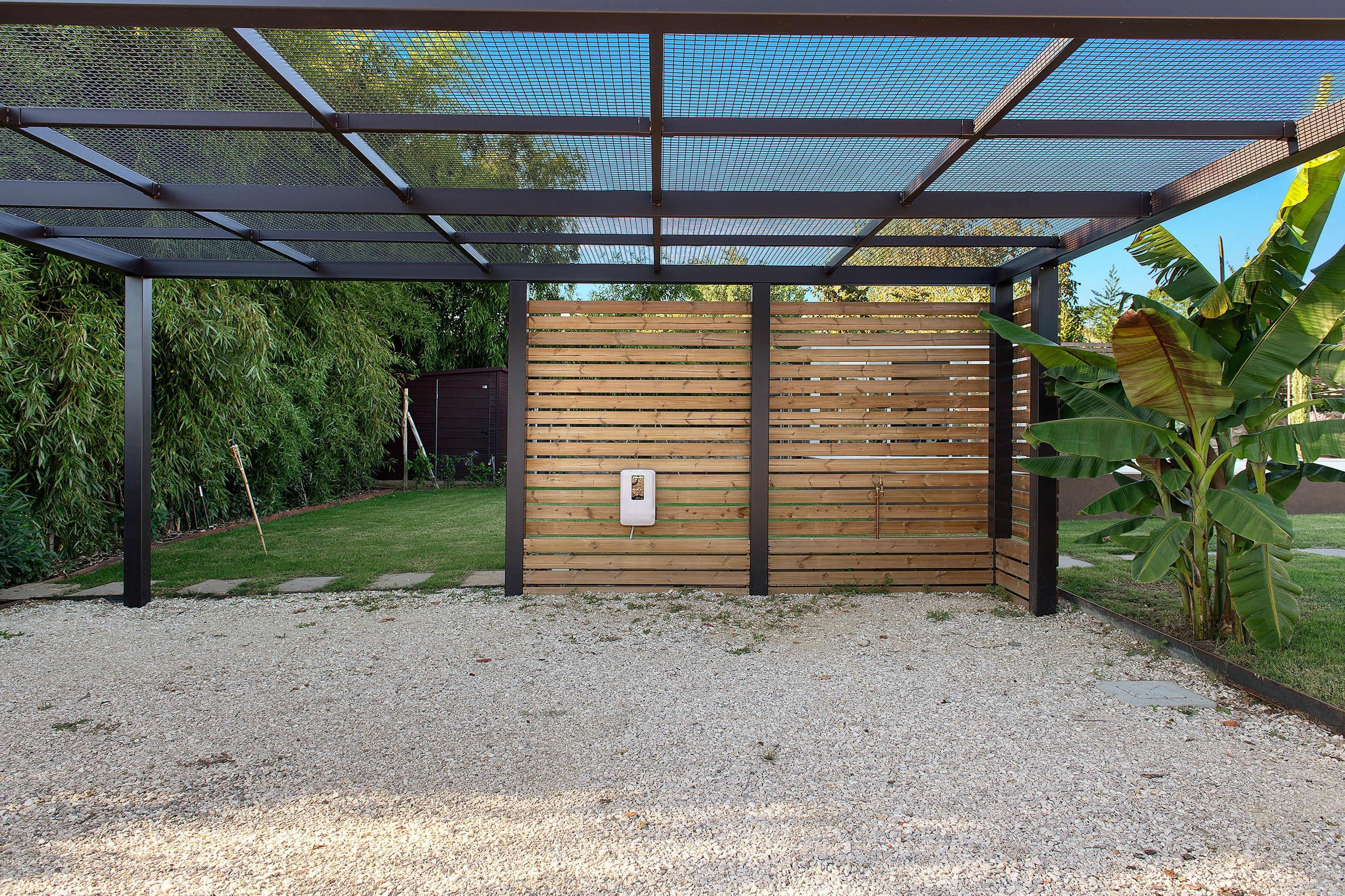 A covered outdoor area with a wooden fence, a metal mesh roof, and a gravel ground.