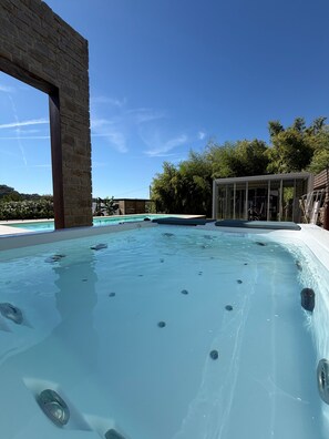 A hot tub with a stone structure and a glass enclosure in a sunny outdoor setting.
