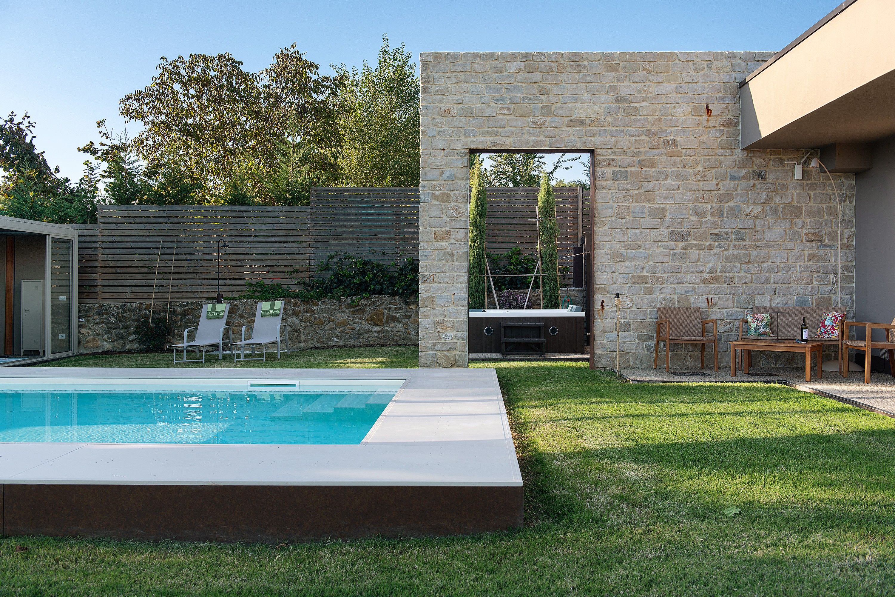 A backyard with a swimming pool, a stone wall, and outdoor furniture.