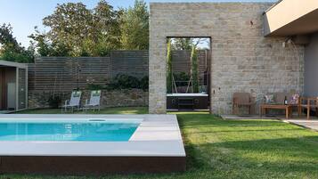 A backyard with a swimming pool, a stone wall, and outdoor furniture.