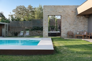 Un pati amb una piscina, un mur de pedra i mobles d'exterior.
