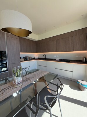 A modern kitchen with a glass dining table, metal chairs, and a pendant light.