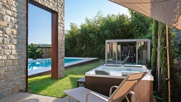 Un muro in pietra, una piscina, una vasca idromassaggio e una sedia a sdraio in un giardino.