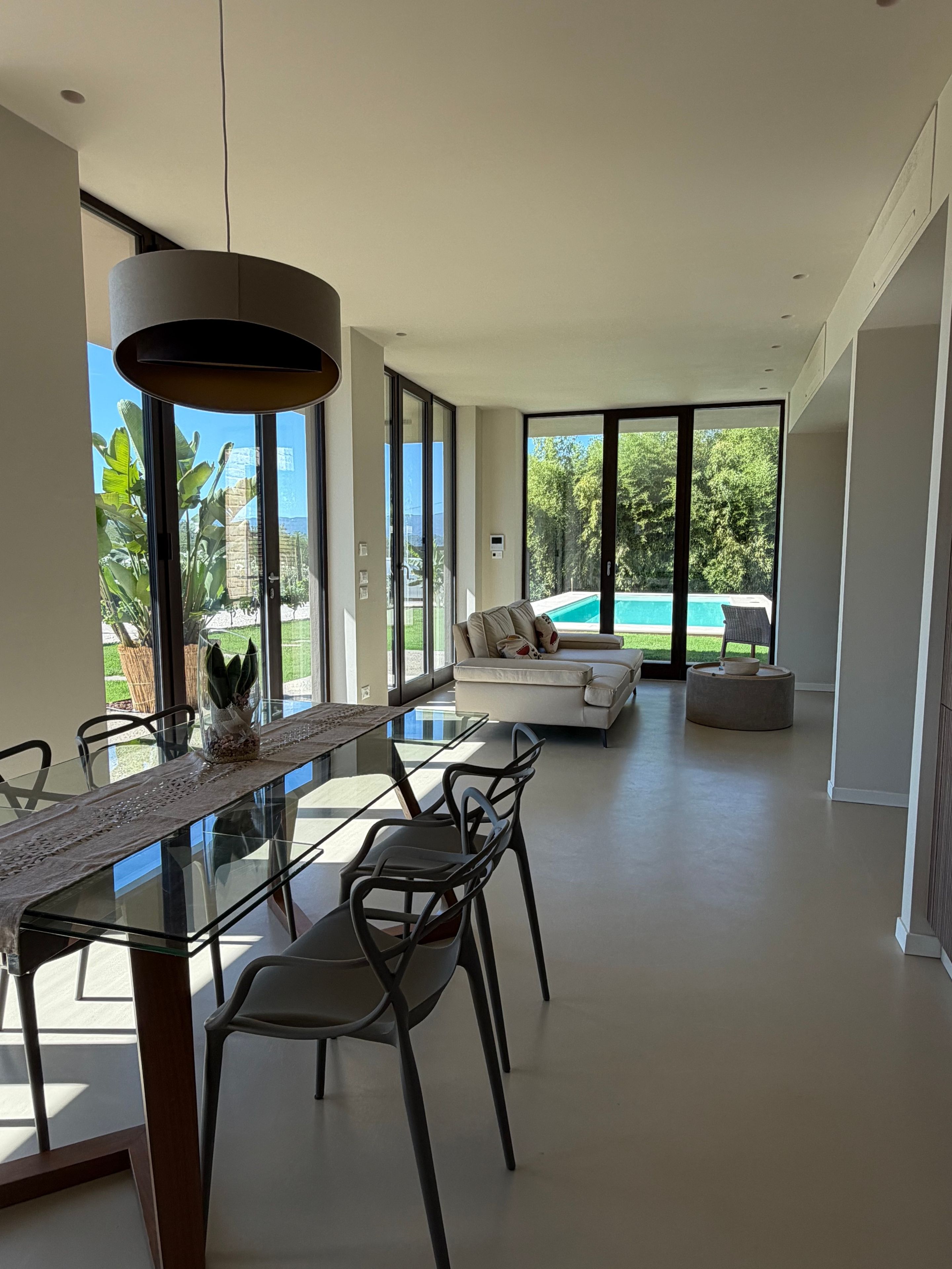 A modern interior with a dining area, sofa, and a view of a swimming pool.