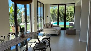A modern interior with a dining area, sofa, and a view of a swimming pool.