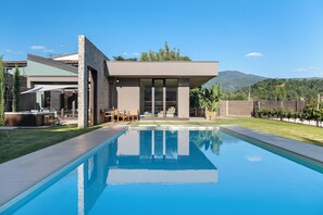 A modern house with a swimming pool, outdoor seating, and a view of mountains.