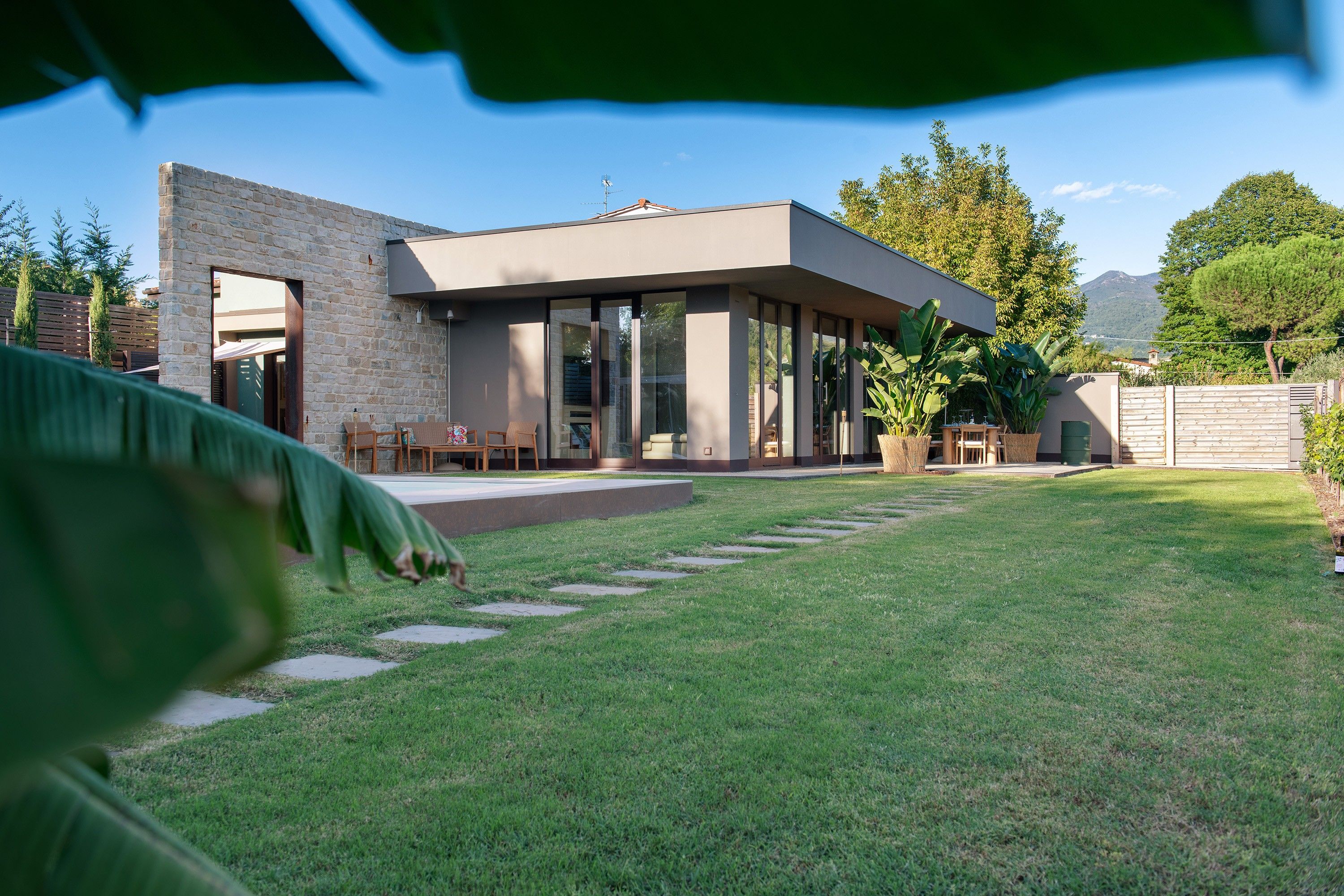 A modern house with a stone facade, a covered patio, and a well-maintained lawn.