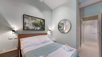 A hotel room with a bed, a wall-mounted TV, a round mirror, and a door leading to another room.
