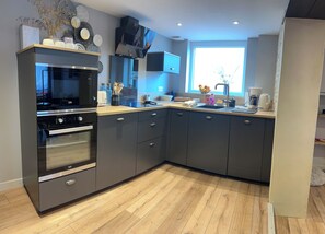 A modern kitchen with grey cabinetry, a built-in oven, and a microwave. - Bois Flotté—downtown—100 meters from the sea—near Bayeux (Port-en-Bessin-Huppain)