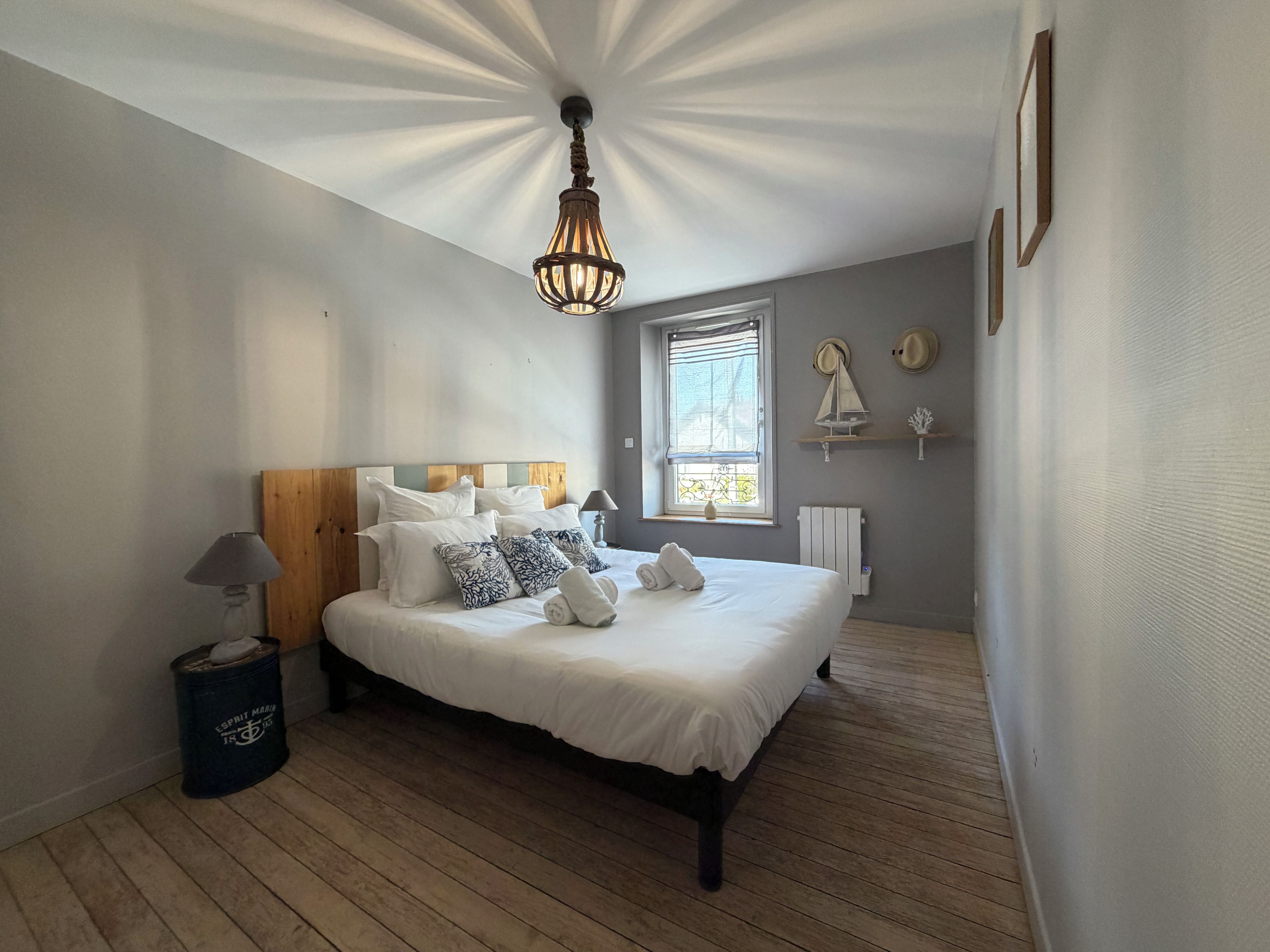 A bedroom with a wooden bed, white bedding, a lamp, a radiator, and a window with a view.