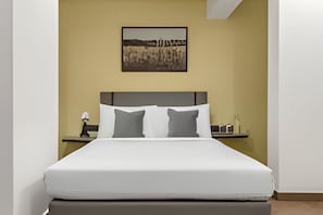 Habitació d'hotel amb un llit, una tauleta de nit, una làmpada i un quadre a la paret.