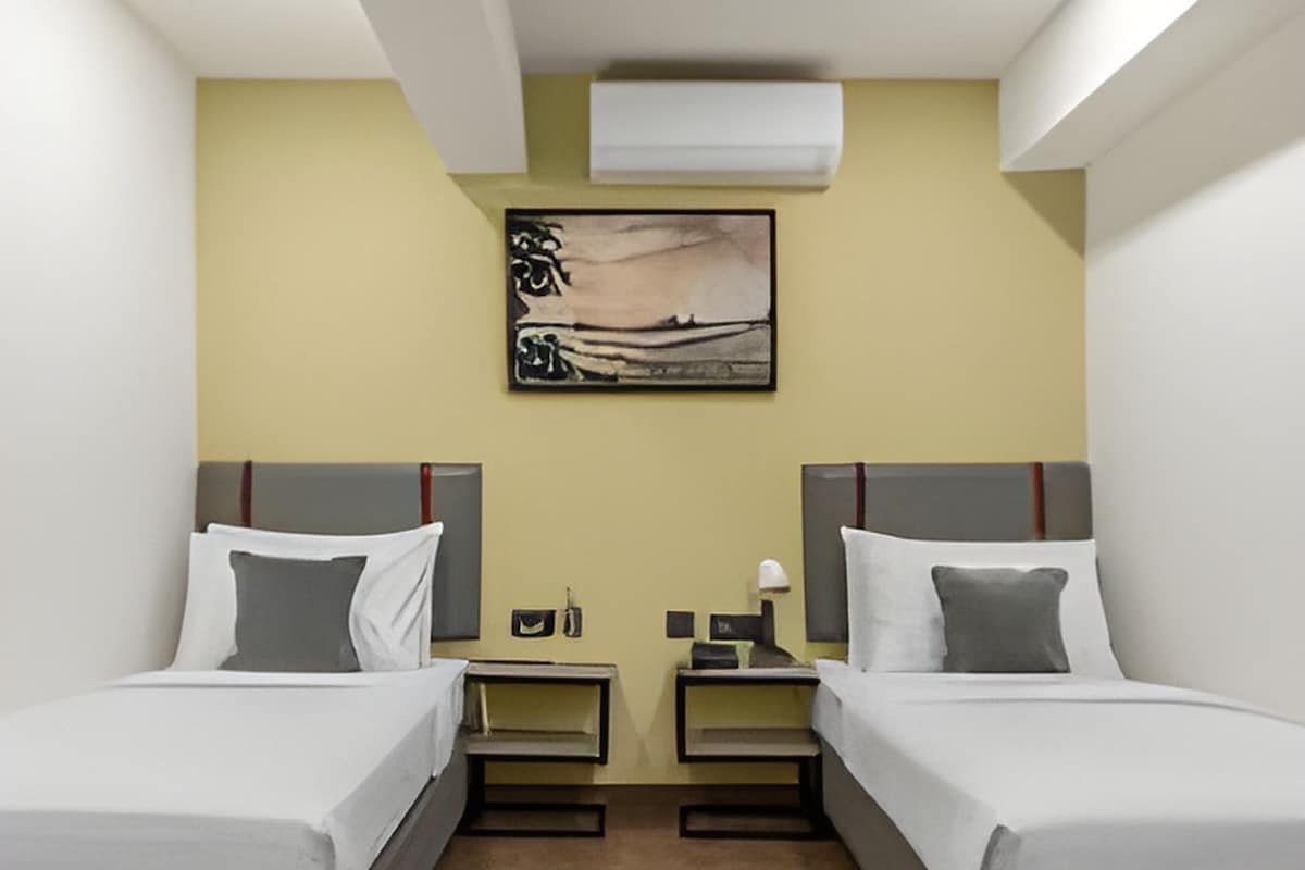 Habitació d'hotel amb dos llits, un quadre a la paret i una tauleta de nit amb una làmpada.