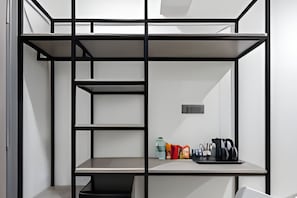 A modern, minimalist room with a built-in desk, shelving, and a small kitchenette area. - Wandr Hotels Richmond Road (Bengaluru)