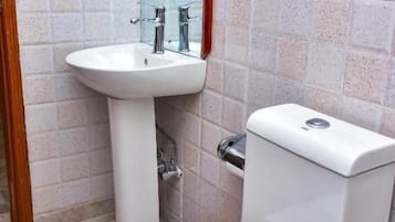 Un baño con inodoro y lavamanos blancos y cabina de ducha de vidrio.