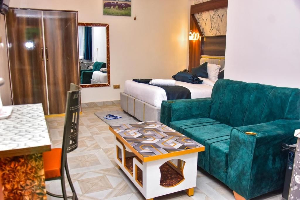 A hotel room with a bed, a green sofa, a small table, a mirror, and a wardrobe.
