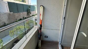 Un balcón con una tabla de snowboard apoyada en la pared, un vidrio y vista de un edificio al otro lado de la calle.