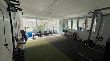 Un gimnasio con equipo de ejercicio, amplias ventanas y una alfombra verde.