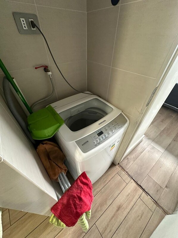 A laundry area with a washing machine, a green basket, and a red towel.