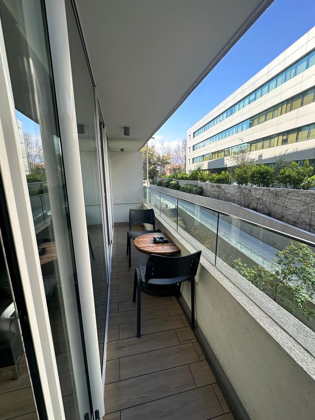 Un balcone con tavolo e sedie, una porta vetrata e vista su un edificio moderno.