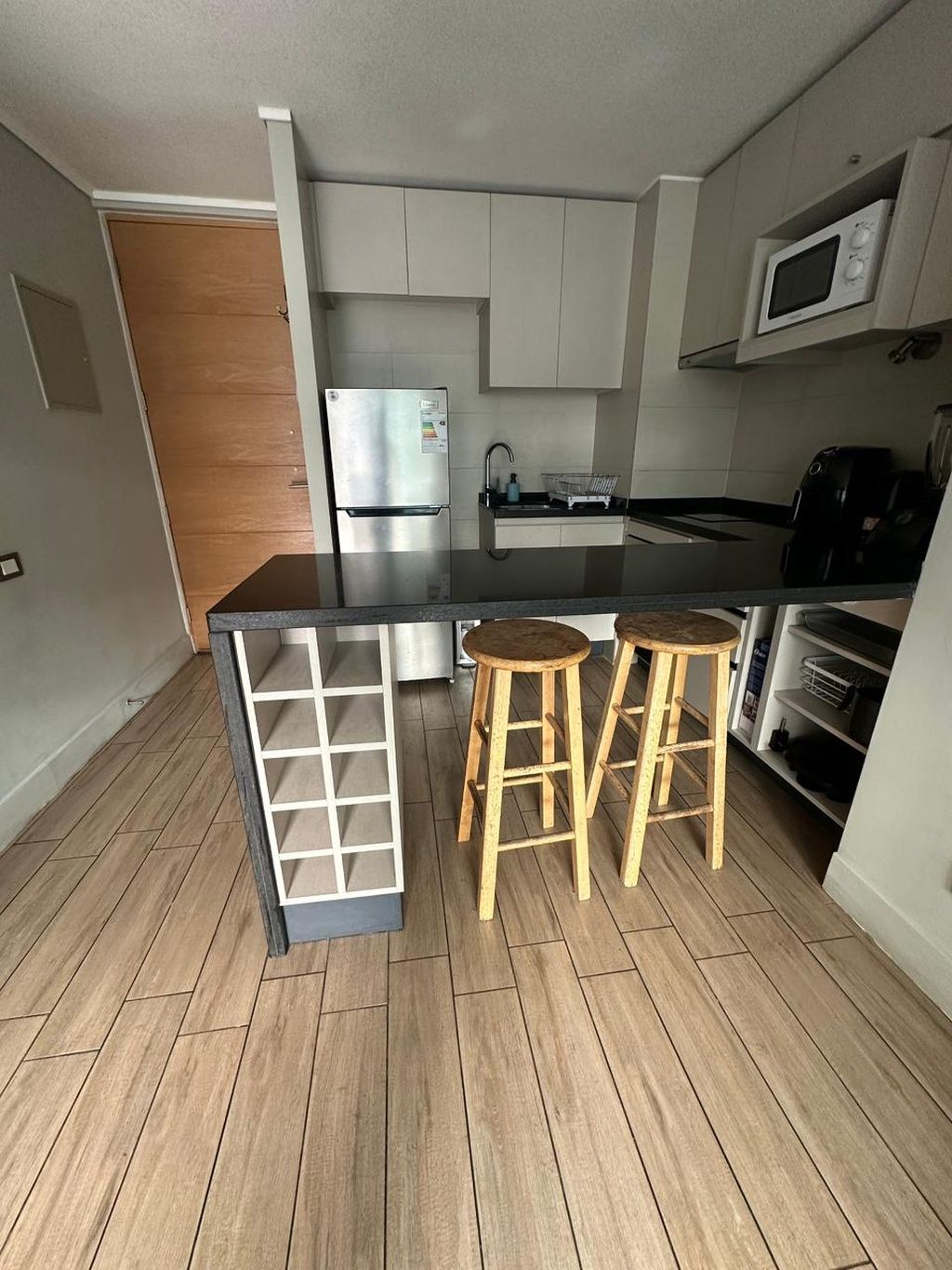 A compact kitchen with a refrigerator, microwave, and wooden stools.