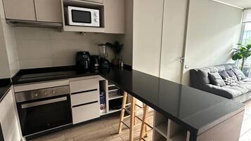 Een moderne keuken met een magnetron, kookplaat en barstoelen.