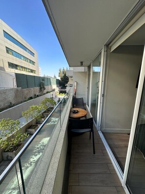 A balcony with a table and chairs, potted plants, and a view of a building across the street.