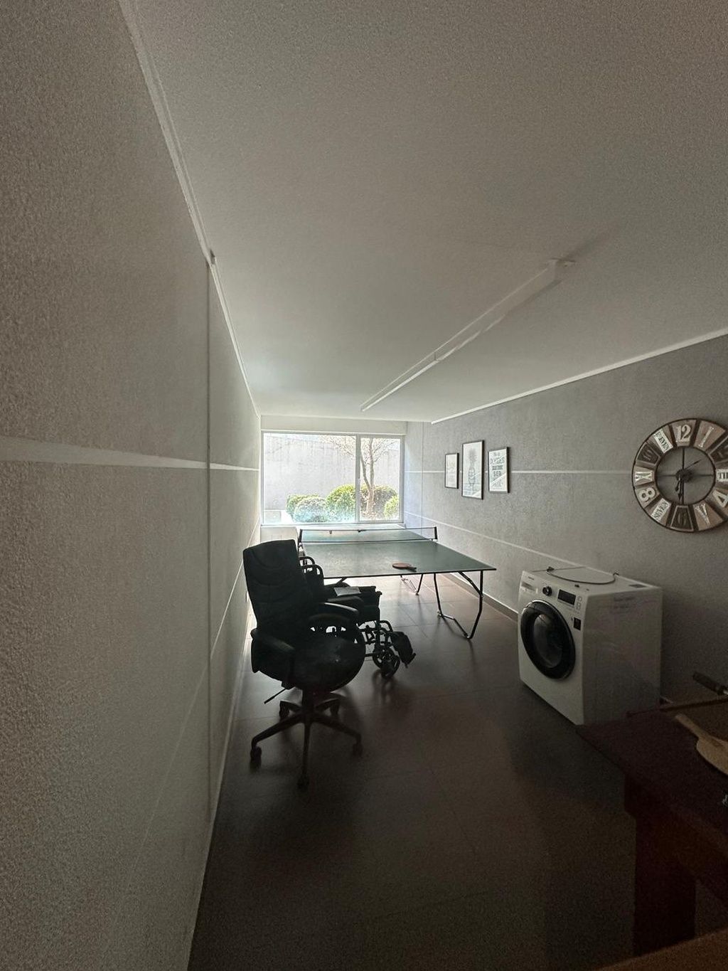 A modern interior with a long hallway, a desk with a chair, a washing machine, and a wall clock.