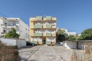 A multi-story residential building with balconies, a car parked in front, and a clear sky.