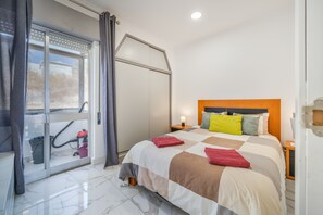 A hotel room with a bed, a window with curtains, a nightstand, and a bathroom with a shower.