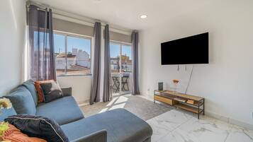 Una sala de estar moderna con un sofá gris, un televisor de pantalla plana montado en la pared y un balcón con vistas a la ciudad.