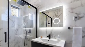 Une salle de bain moderne avec une douche à parois de verre, un meuble-lavabo blanc et un miroir doté d’un éclairage circulaire.