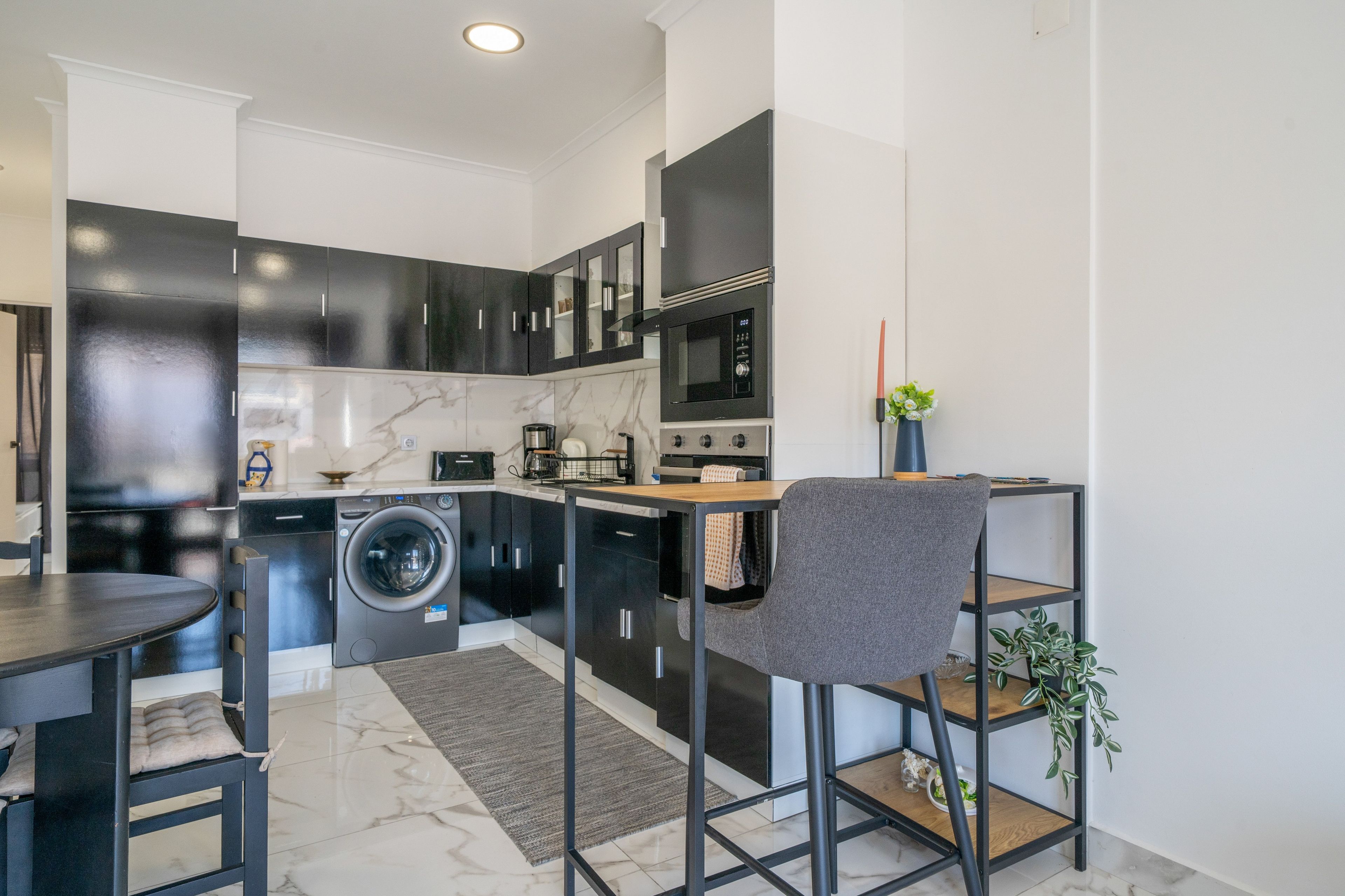 Una cocina moderna con lavadora integrada, microondas y comedor con mesa y sillas.