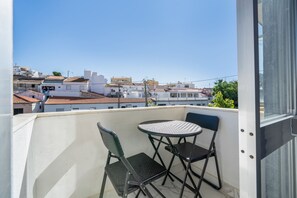 Un balcon avec une table et deux chaises, donnant sur un quartier résidentiel avec des immeubles et un ciel dégagé.