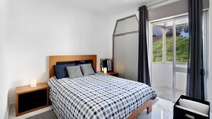 Une chambre à coucher moderne, avec un lit, des tables de chevet, une lampe et une vue sur la verdure par la fenêtre.