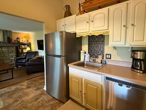 A kitchen with a stainless steel refrigerator, white cabinets, a stone wall, and a coffee maker. - Woodland Mountain Retreat | Walk to Sugar Mountain Lodge | Private Balcony (Sugar Mountain)