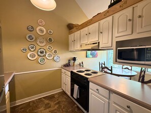 A kitchen with white cabinets, a stove, an oven, a microwave, and a wall decorated with plates. - Woodland Mountain Retreat | Walk to Sugar Mountain Lodge | Private Balcony (Sugar Mountain)