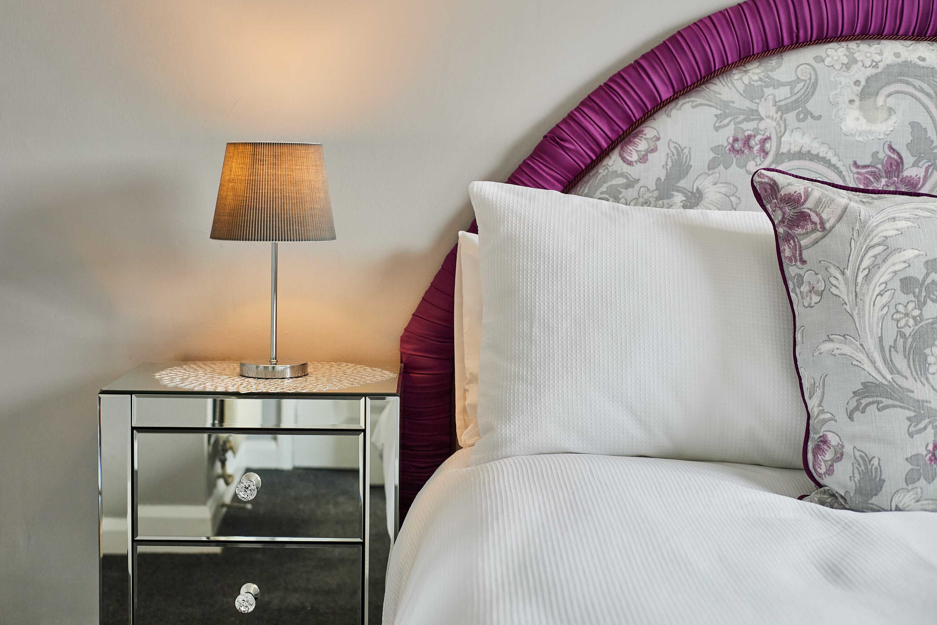 A neatly made bed with a white pillow and a decorative pillow with a floral pattern.
