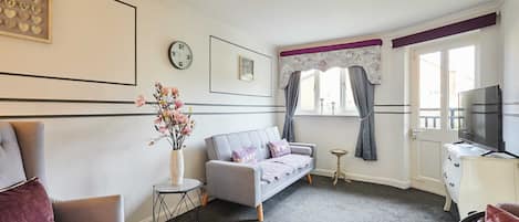 A living room with a sofa, armchairs, a small side table, a vase with flowers, a clock, and a television on a cabinet.