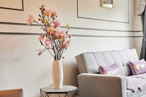 A room with a grey sofa, a round side table with a white vase containing pink flowers, and a framed picture on the wall. - Host & Stay | Theatre View (Darlington)