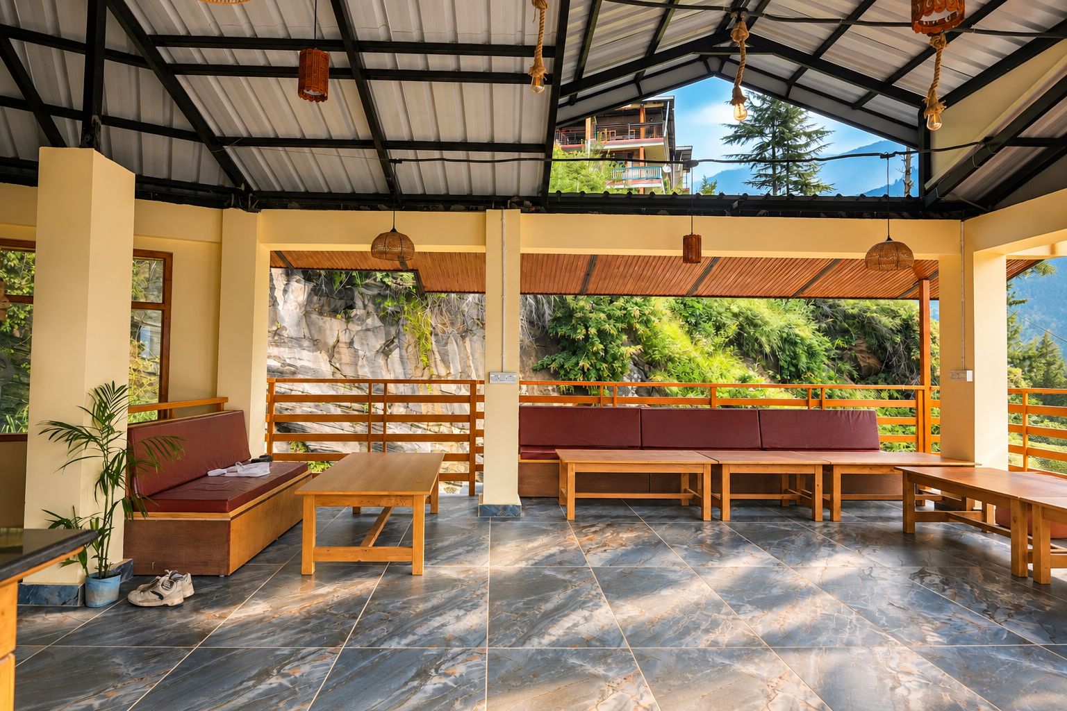 A spacious indoor area with a high ceiling, wooden benches, a table, and a view of a mountainous landscape through large windows.