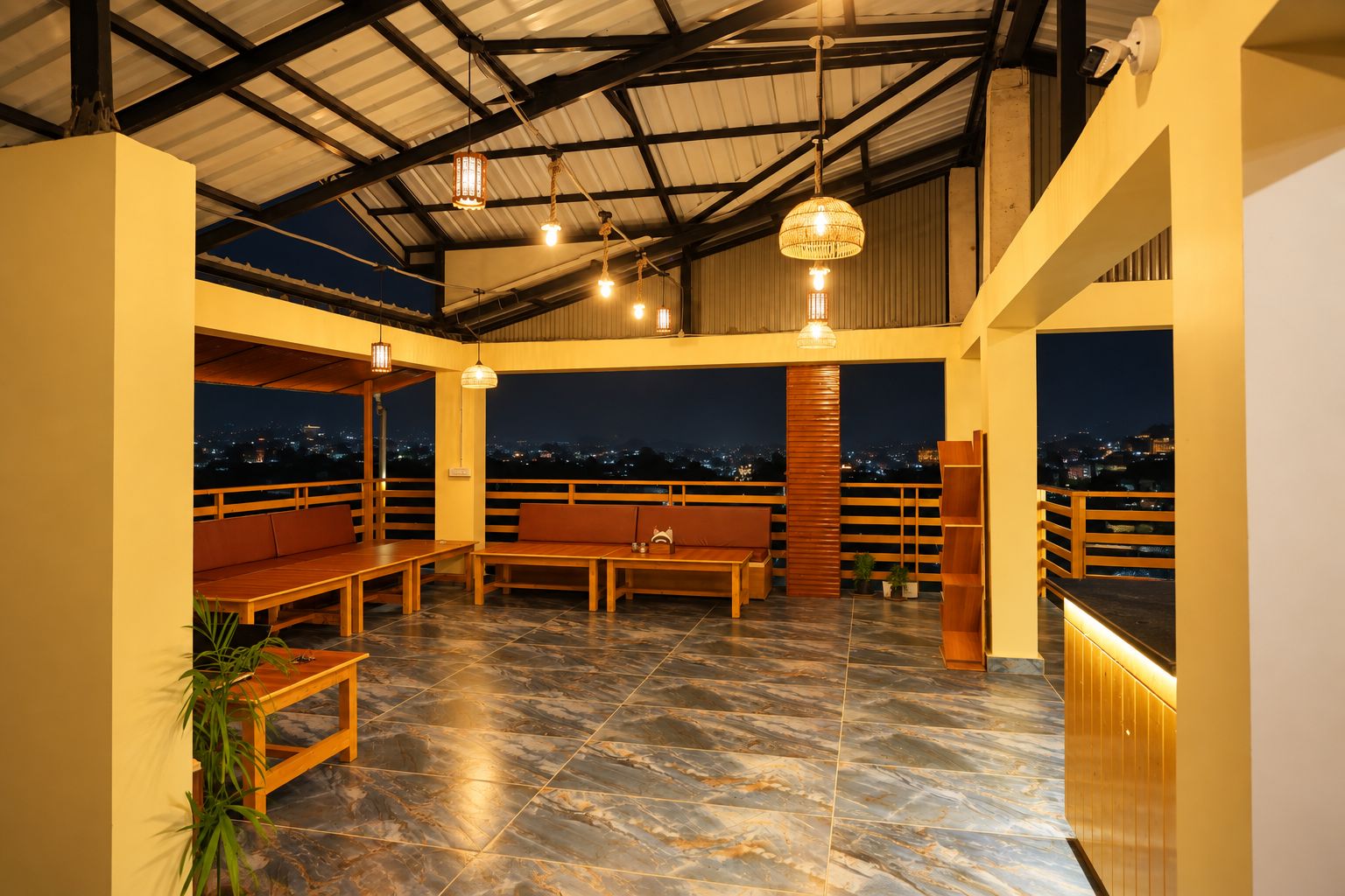 Una terraza en la azotea con mobiliario, vistas de la ciudad de noche y una cámara de seguridad.