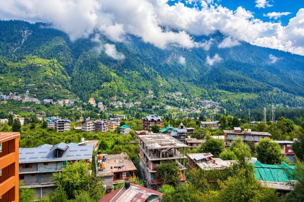 A mountainous town with buildings surrounded by lush greenery and clouds. - Echo Homestay (Manali)