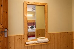 A wooden-framed mirror with a built-in shelf for towels, a bed with a headboard, and a door with a handle.