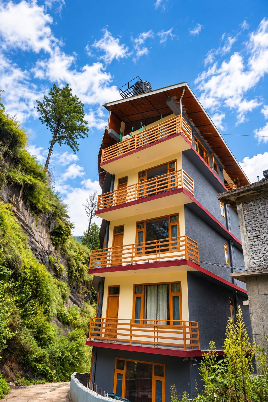 A multi-story building with balconies, set against a backdrop of greenery and a clear sky.