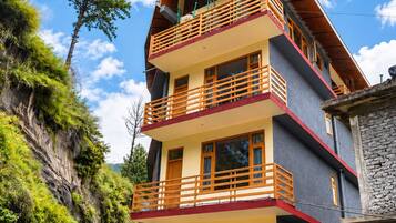 A multi-story building with balconies, set against a backdrop of greenery and a clear sky.