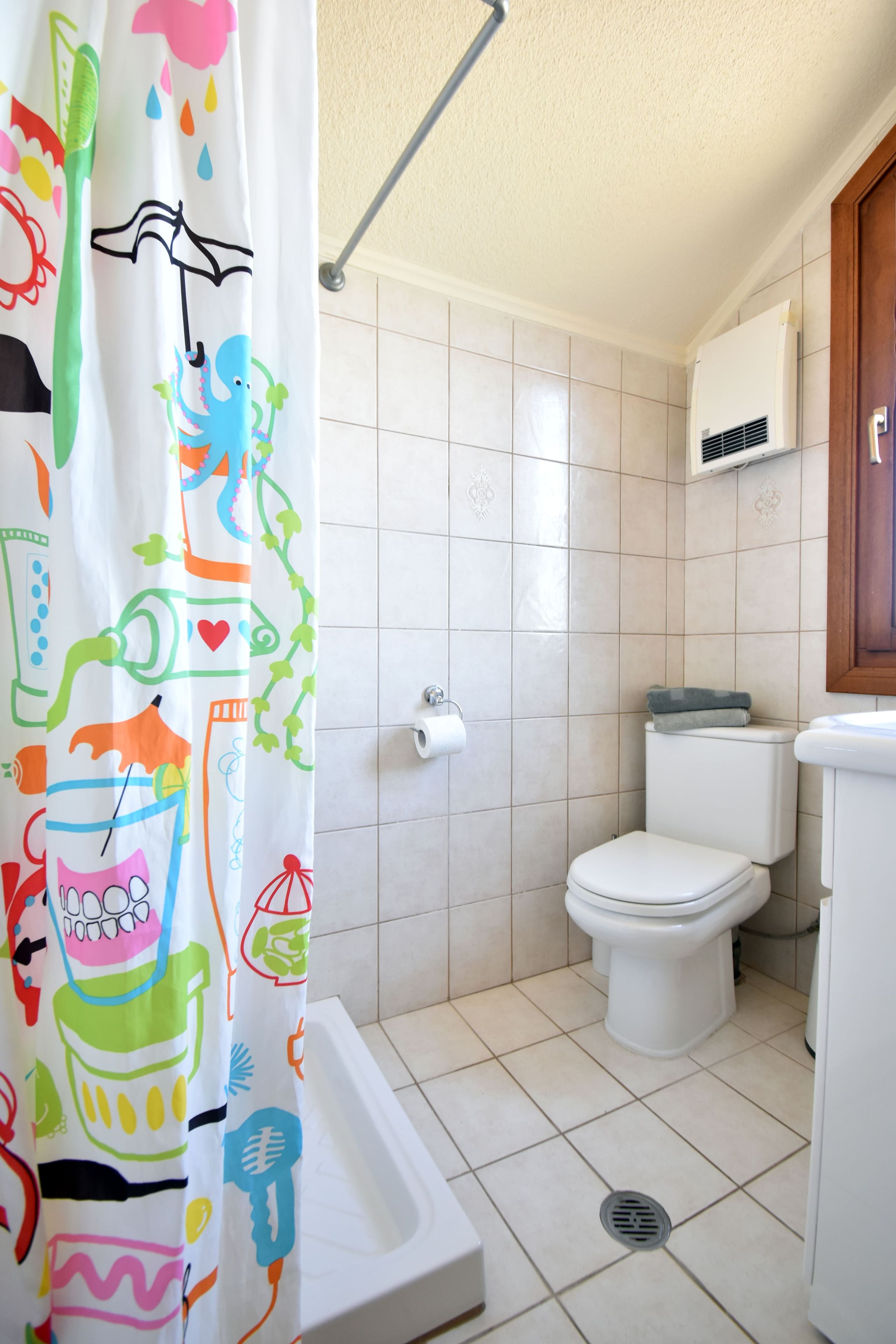 A bathroom with a shower curtain featuring colorful patterns, a toilet, a bidet, and a wall-mounted air conditioner.