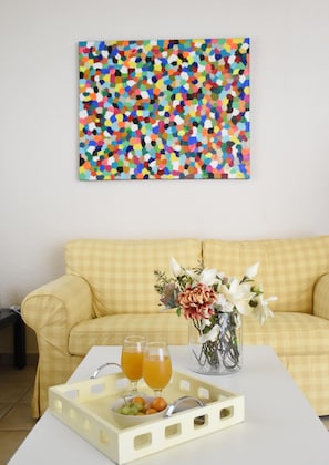 A room with a yellow checkered sofa, a white coffee table with a fruit tray, two glasses of orange juice, and a vase with flowers. - Villa Paradiso - Your Summer Sanctuary in Sani (Sane)