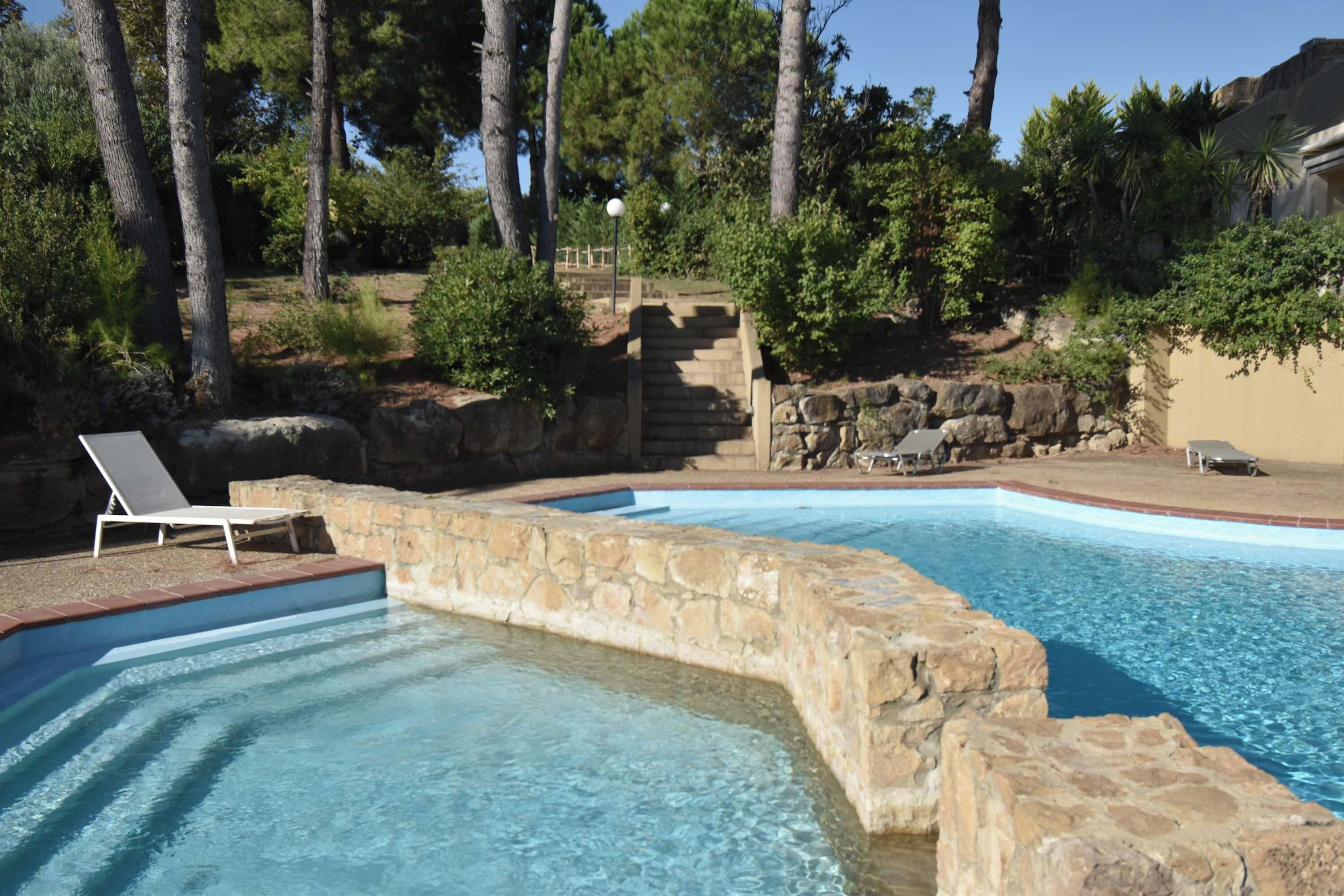 A swimming pool with a stone border, surrounded by trees and a stone wall.