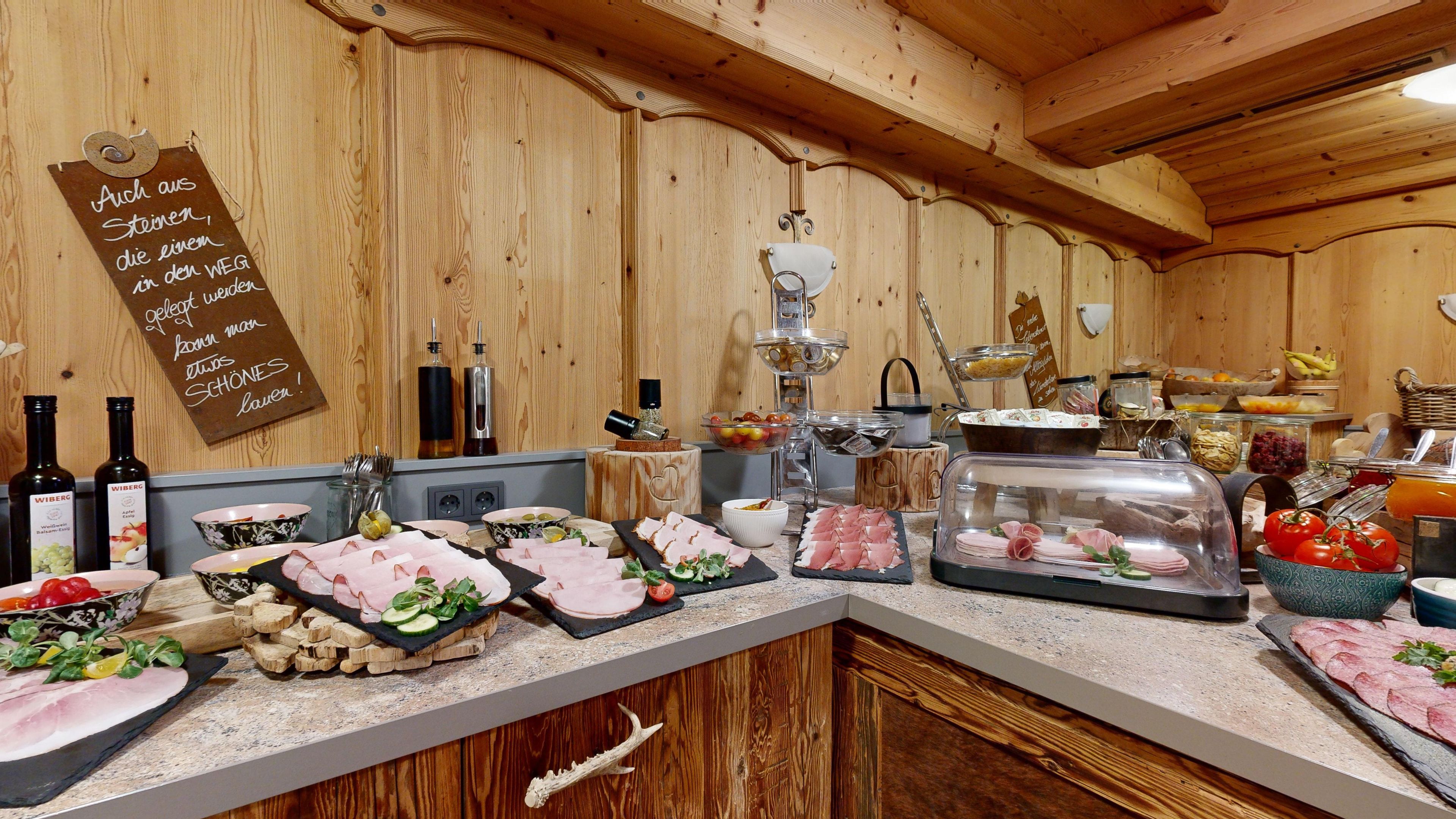 Ein Holzinterieur mit einer aufgebauten Speiseauslage, darunter verschiedene Fleisch-, Käse- und Obstsorten.