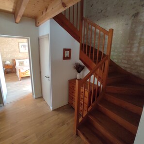 A wooden staircase with a handrail leading to a room with a white door and a small wooden dresser.